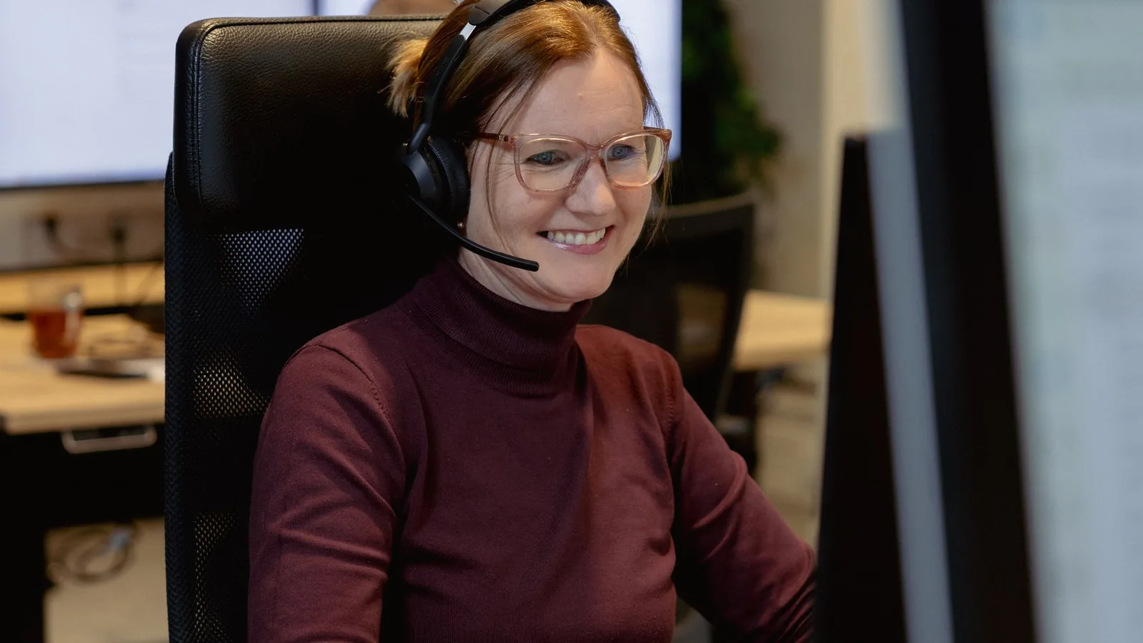 Medewerker met headset achter haar bureau, in gesprek met een klant